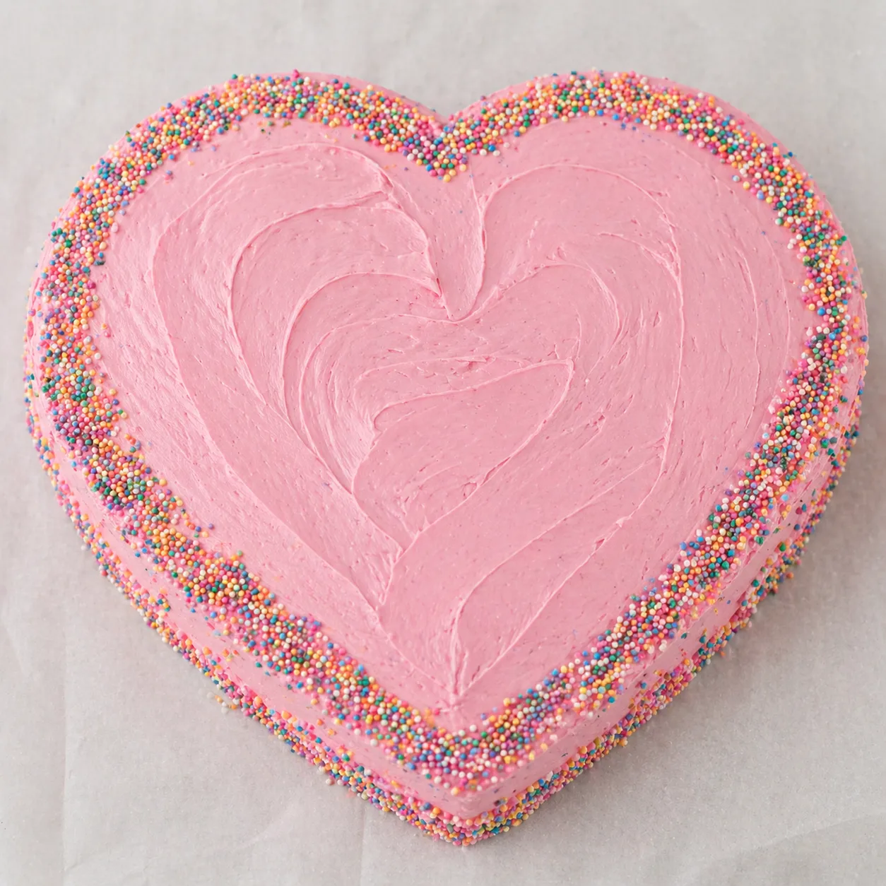 Heart-shaped pink buttercream cake with fresh strawberries on white marble in soft natural light, romantic dessert