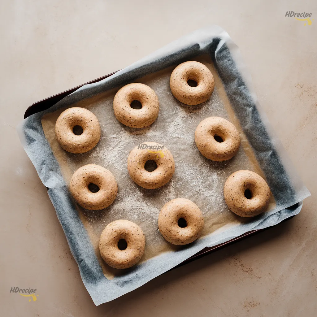 gluten-free-bagels-shaping Top-down view of raw gluten-free bagels being shaped on a parchment-lined baking sheet.
